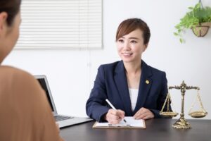 Lilyのカウンセリングで女性弁護士が笑顔で書類に記入、天秤のオブジェとノートPCも見える