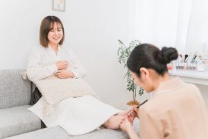 Beauty Salon Lilyでソファに座りフットネイルをしてもらい笑顔の女性