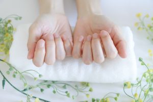 Beauty Salon Lilyのハンドケア。白いタオルに置かれた女性の両手と周りの花々