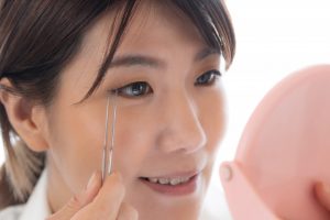Lily+eyeで鏡を見ながらピンセットでまつ毛を整える若い女性