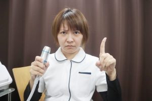 Beauty Salon Lilyの店員が美顔器を持ち、人差し指を立てて注意を促す